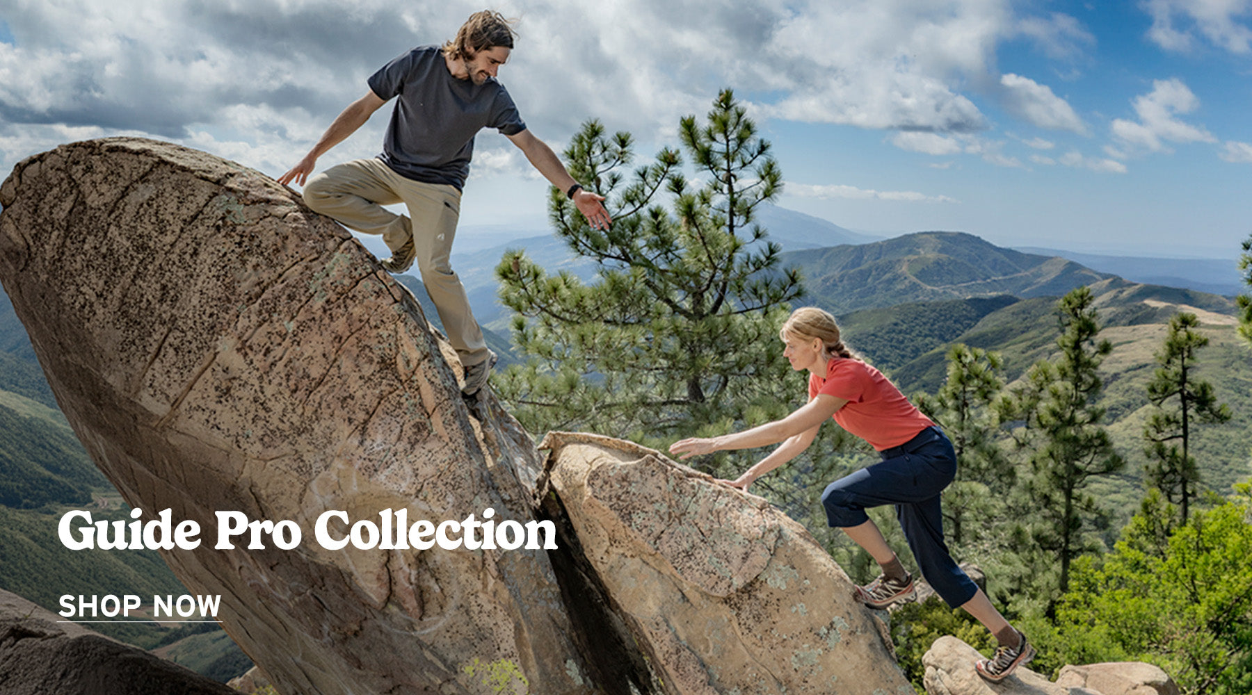A man and woman climbing large rocks along a mountain ridge, both wearing technical hiking pants with the words Guide Pro Collection Shop Now displayed in the lower left side of the image