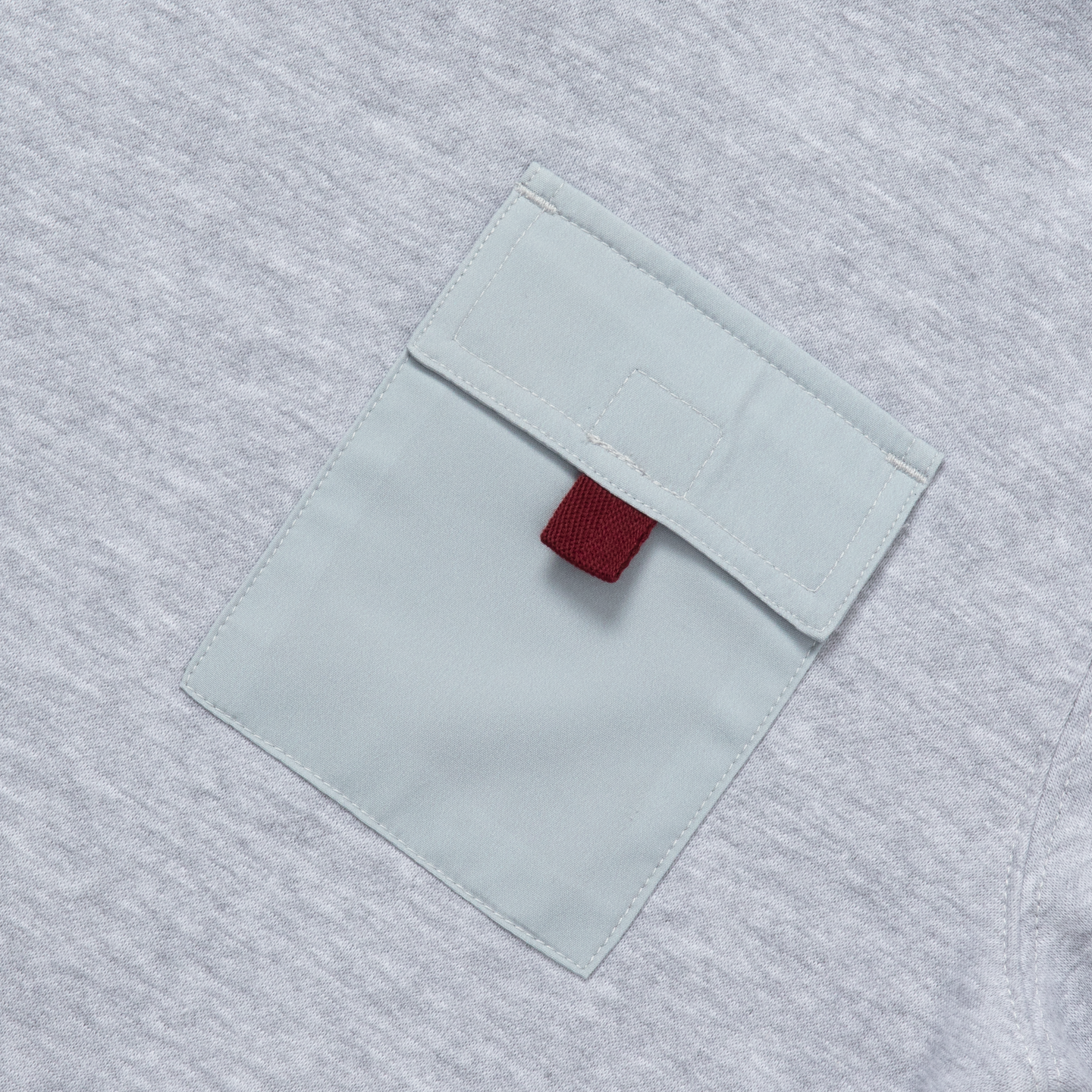 Gray fleece crewneck with white chest pocket and maroon fabric detail on gray textured background.