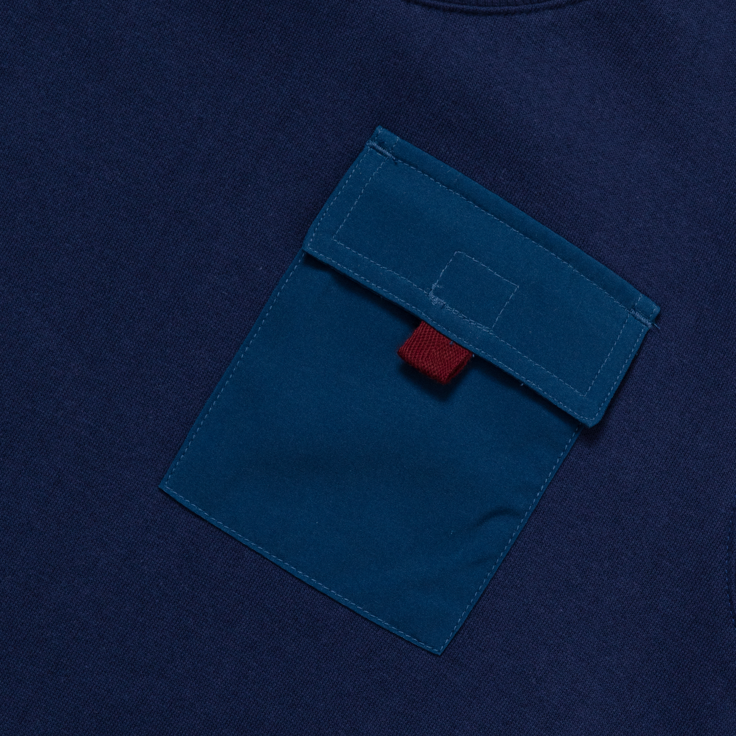 Navy fleece crewneck with teal front pocket and red label detail.