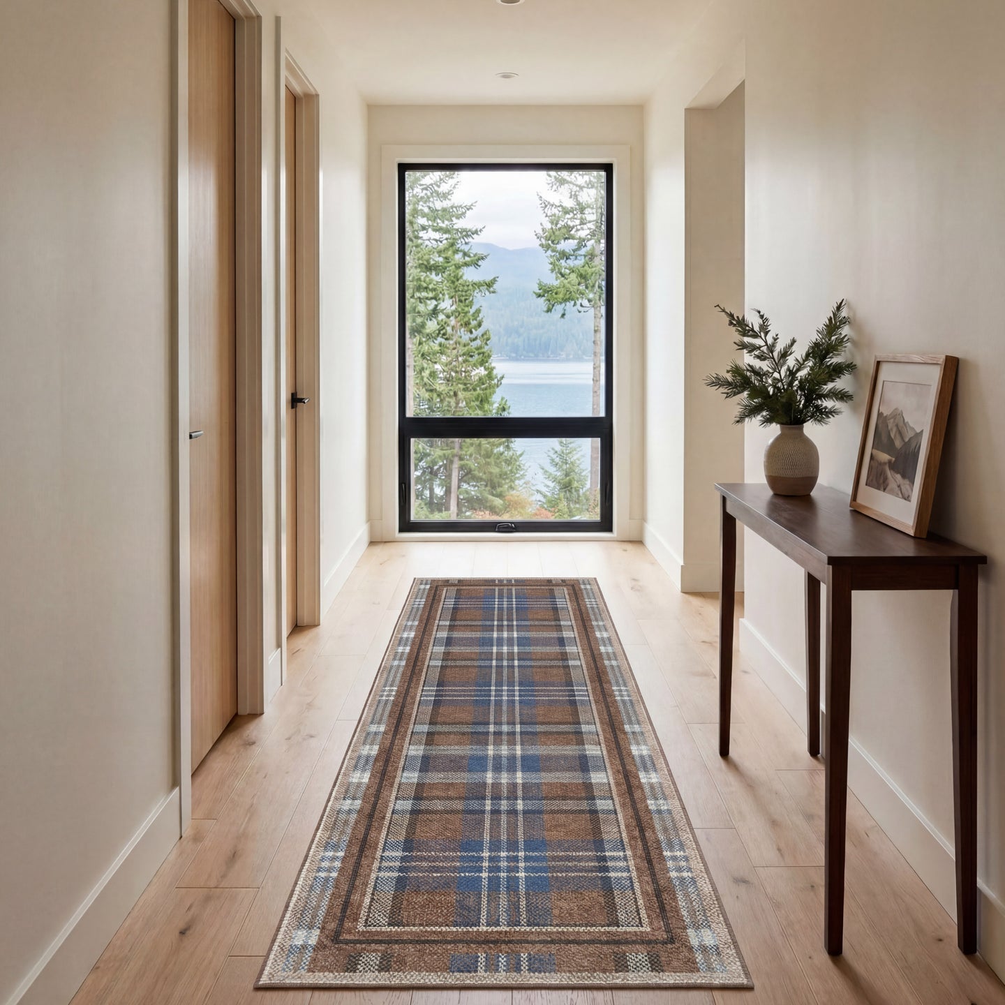 Hallway with a plaid runner rug, wooden floor, and a view of trees and water through a window.