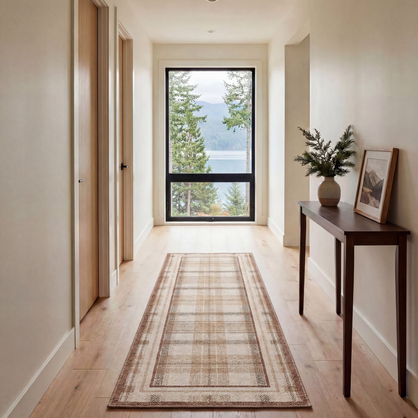 Hallway with a long rectangular rug, wooden console table, and large window overlooking trees and water.