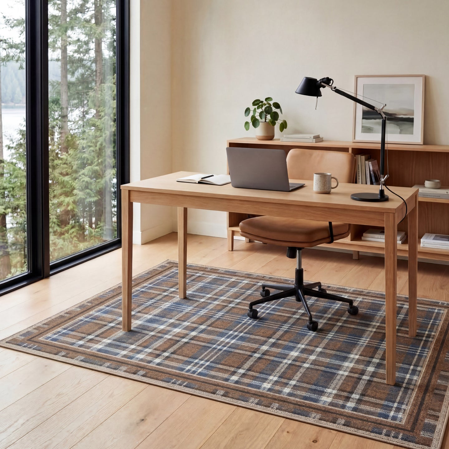 Home office with wooden desk, chair, laptop, and decor items on a plaid rug.