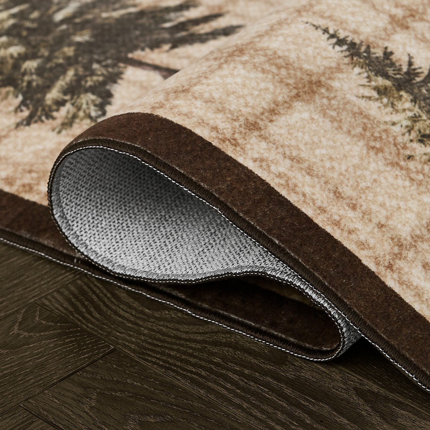 Rolled area rug with beige and brown tones featuring pine tree motifs, showing gray backing and stitched edge.